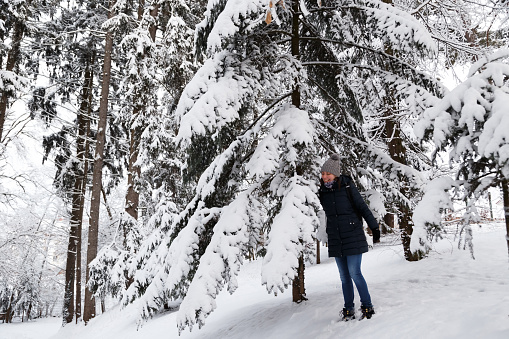 Young smiling woman standing near to fir tree in snow-covered winter forest. Snowy winter.