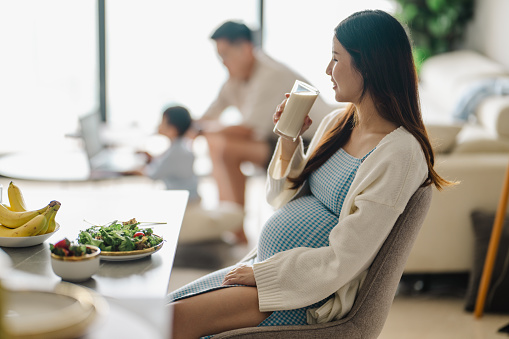 Beautiful Asian Pregnant Woman Drinking a Glass of Milk for Health Care at home.