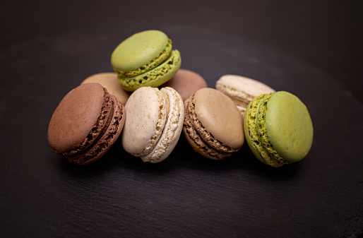 Macarons in beige, brown, pistachio and cream colors on a black slate background. Close-up in different positions. Selective focus.
