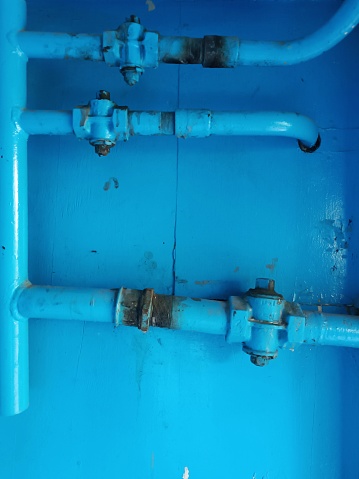 Very old dirty blue Pipe construction. Vertical and horizontal pipes with connecting elements. Blue gas pipes, connecting element at blue wall. Gas equipment Part. Free focus. Indoor Gas Line.