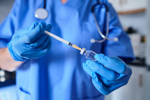 Front view of unrecognizable nurse in blue uniform filling syringe.