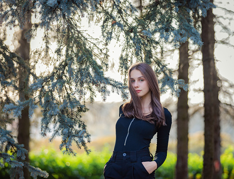 A girl stands near a blue spruce in an autumn park