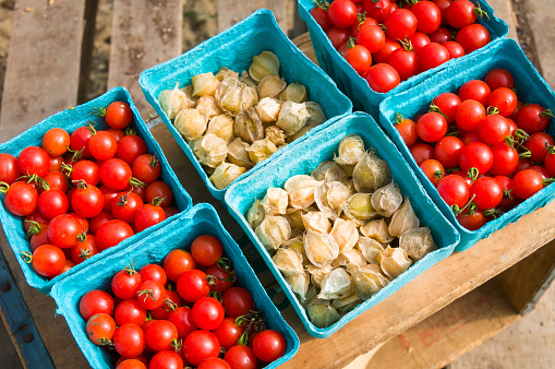 Blue Paperboard baskets of Cape gooseberry (Physalis peruviana) and ripe, red cherry tomatoes on wooden background at a Cape Cod farmers market.