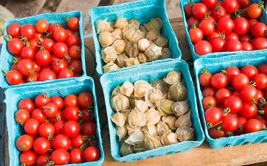 Blue Paperboard baskets of Cape gooseberry (Physalis peruviana) and ripe, red cherry tomatoes on wooden background at a Cape Cod farmers market.