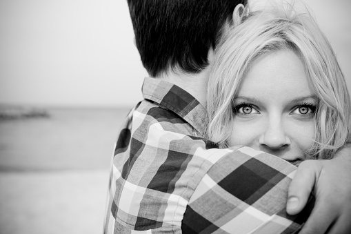 Close-up of young couple emracing on the beach. Beautiful content woman looking at camera. Black and white image.