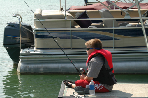 A boy fishing on a boat dock in the summer.