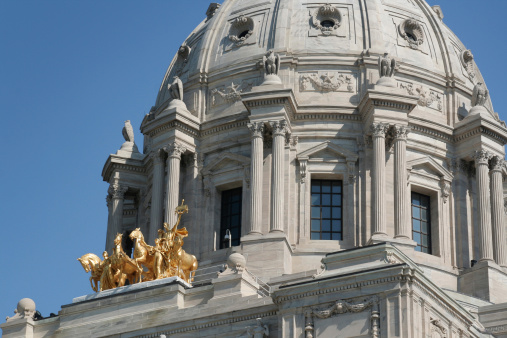 Building exterior detail of the tate of Minnesota Capitol dome, a close-up of the state government building in St. Paul, Minnesota, USA. A gold statue of horses decorates the facade of the grand architecture.
