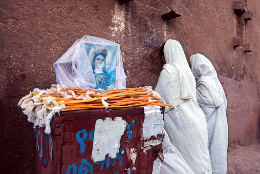 Lalibela. Ethiopia-mars 25-2018:Two Orthodox Christian ladies dressed in white robes pray outside the church of Saint Gabriel. The 11 medieval monolithic cave churches of this 13th-century 'New Jerusalem' are situated in a mountainous region in the heart of Ethiopia near a traditional village with circular-shaped dwellings. Lalibela is a high place of Ethiopian Christianity, still today a place of pilmigrage and devotion.