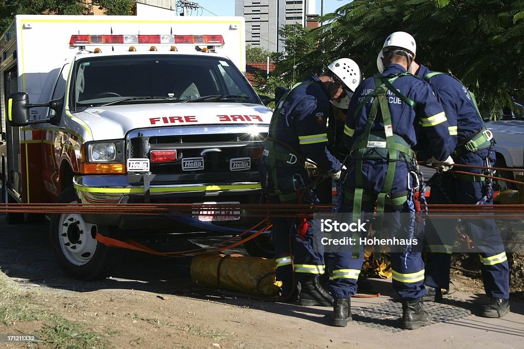 emergency tow emergency workers attach cables to rescue vehicle with trees and building in backgroundsee also ... Group Of People Stock Photo