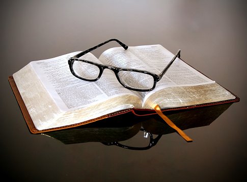 An open bible with reading glasses sitting on it.