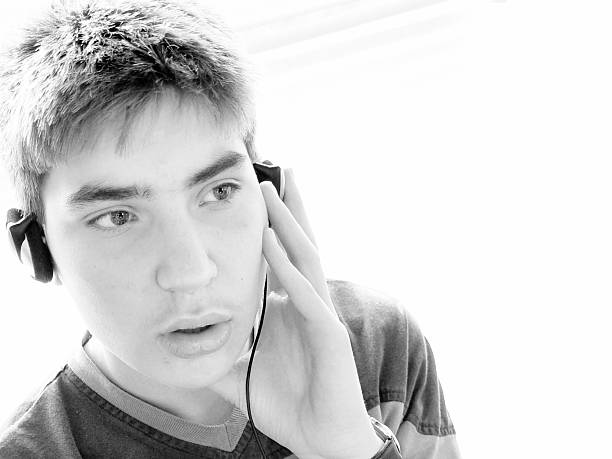 Handsome young hipster man in stylish clothes sitting on a park bench with skateboard on the bench,he is listening music on his mobile phone, on a lovely autumn day. black and white photo