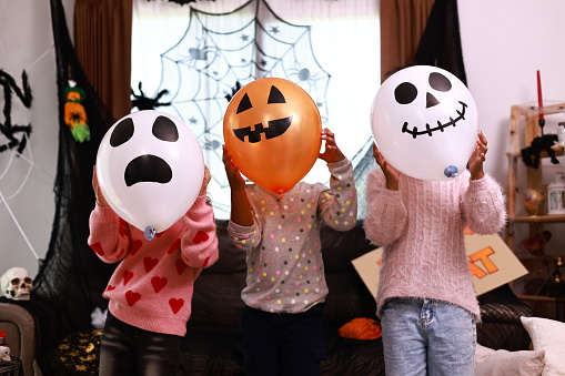 group of children holding a balloon they drew a ghost on, in front of their face