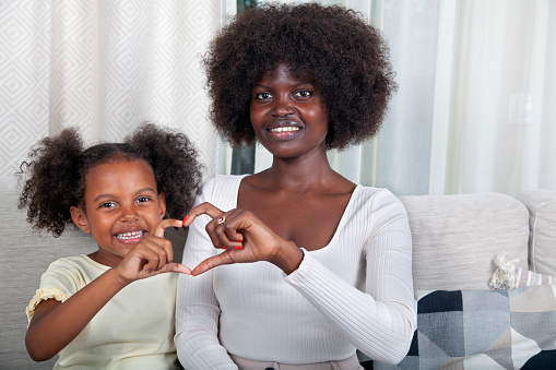 Happy mother and daughter making a heart sign with their hands at home