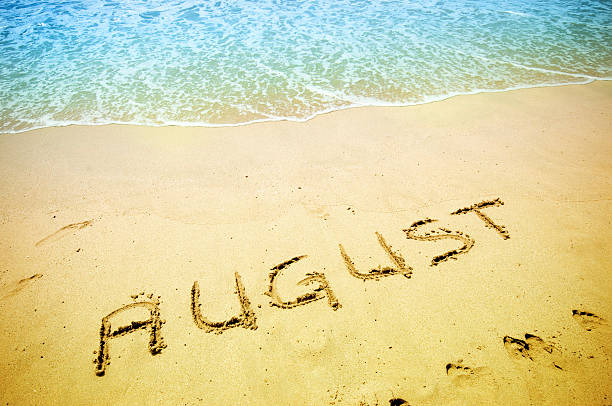 August handwritten in the sandy shoreline August written on the sand of a beautiful tropical beach. Visible are one island in the sea, turquoise water, little splashy waves, golden sand and beautiful cloudscape over the sea. august stock pictures, royalty-free photos & images
