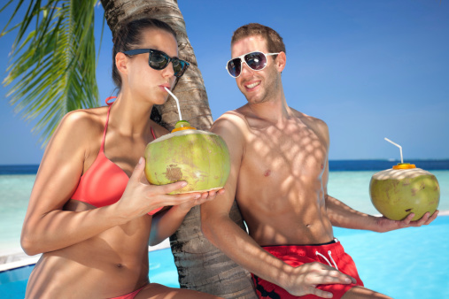 young couple with fresh coconuts drinking at poolside