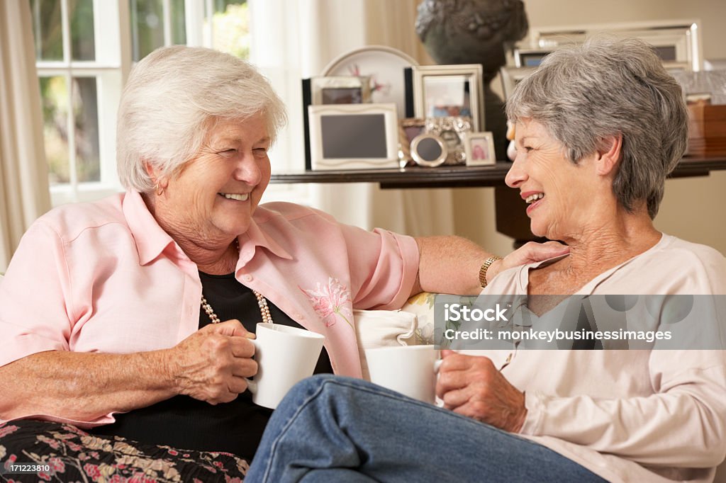 Two Retired Senior Female Friends Sitting On Sofa Two Retired Senior Female Friends Sitting On Sofa Drinking Tea At Home Having A Laugh Drinking Stock Photo