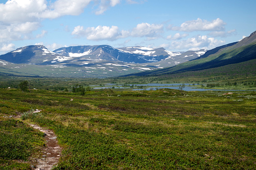 Lake in subarctic terrain of Lapland wilderness with mountains and blue sky with cumulus clouds in the background