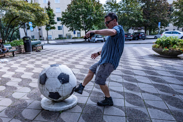 Stockholm, Sweden Sept 11, 2023 A man pretends to kick a large soccer ball used on a plaza to block cars in the Vastra Skogen district.