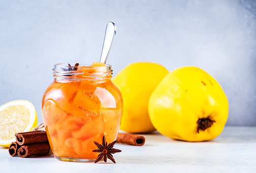 Autumn Quince jam or confiture in glass jar with cinnamon and anise on gray table background