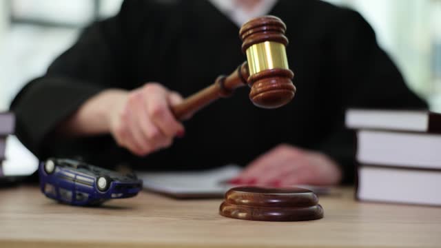 Judge knocking with gavel at table with overturned toy car