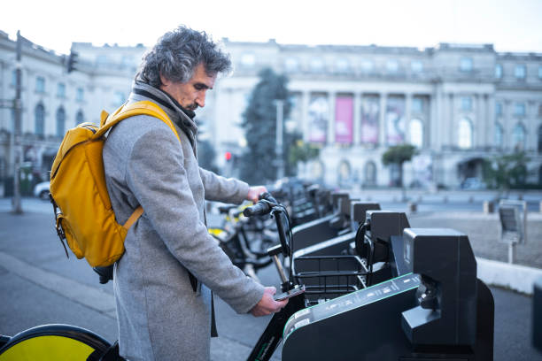 Sustainable urban mobility. Man renting city bike. Sustainability in everyday urban life. Renting a bike from shared bike station with smartphone by scanning QR code. bucharest people stock pictures, royalty-free photos & images