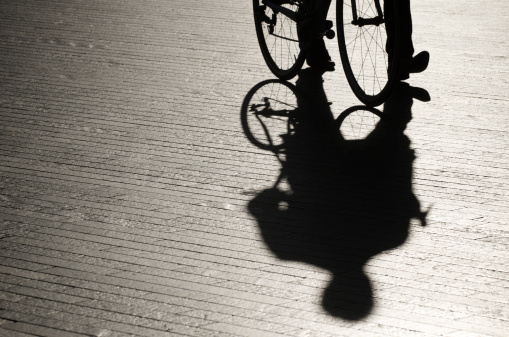 Shadow figure walks with shadow bicycle on bright modern pavement background