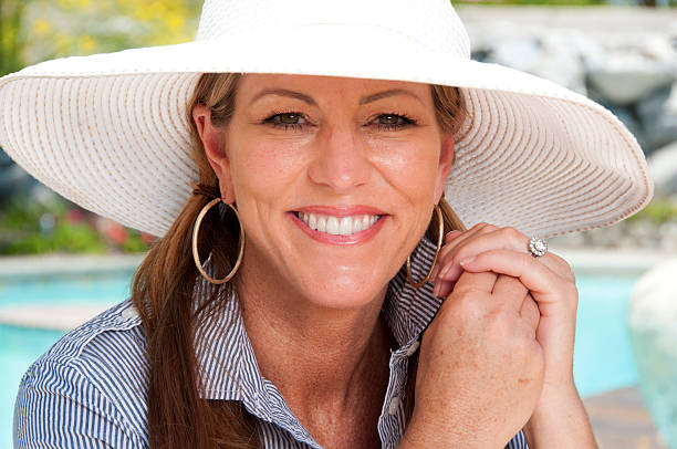 Attractive Mature Woman Wearing Sun Hat An attractive, mature woman in her 40s, poses for the camera. She is wearing a sun hat and smiling. hoop earring stock pictures, royalty-free photos & images