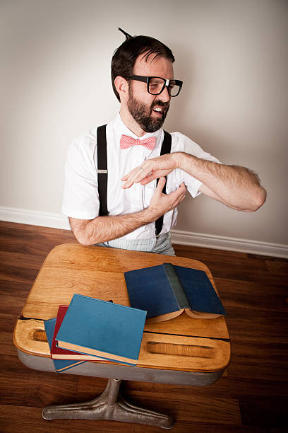 nerd człowiek drapanie jego pacha, gdy siedzi przy biurku szkoły - desk men bizarre classroom zdjęcia i obrazy z banku zdjęć