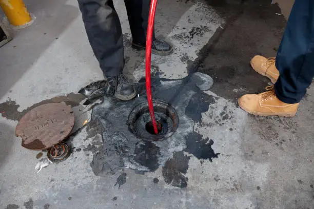 Commercial plumbers hydro line jet a pipe at a large restaurant. Grease can be seen on the pavement surrounding the pipe.