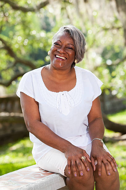 Portrait of mature African American woman Portrait of mature African American woman (50s) sitting outdoors in park. hand on knee stock pictures, royalty-free photos & images