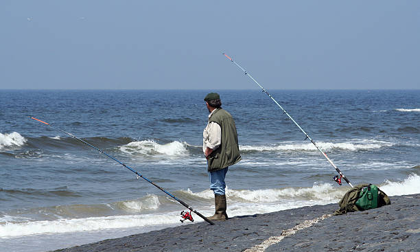 Standing fisherman with two rods, fishing in the sea A standing fisherman with two rods, fishing in the sea hook of holland stock pictures, royalty-free photos & images