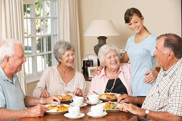 gruppo di senior coppie godendo pasto insieme adolescente helper - nursing home senior adult group of people home caregiver foto e immagini stock