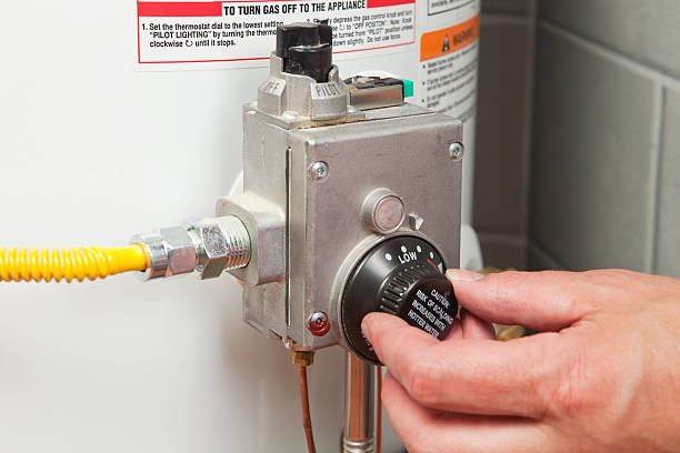 Hand Turning Down Water Heater Thermostat "A male hand is turning down the temperature on a gas water heater's thermostat. This is a measure of energy conservation which requires less gas to be consumed heating the stored water. Additionally, this could serve as a home safety image, by turning down the temperature the risk of scalding is reduced." boiler stock pictures, royalty-free photos & images