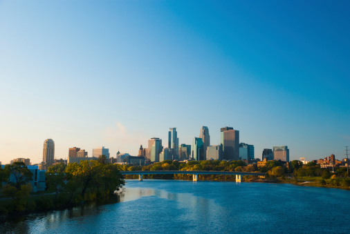 Downtown Minneapolis skyline in the Morning with a bridge midway and the Mississippi River in the foreground.