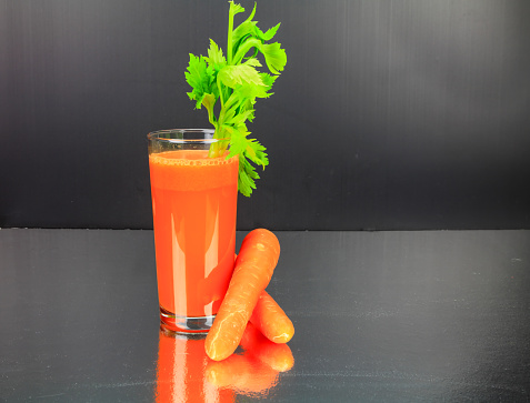 Carrot juice with celery in a glass on a sainless steel bench top