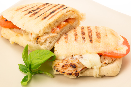 Toasted Chicken, tomato and mozzarella Panini sandwich that has been cut in half and placed on a plate - studio shot