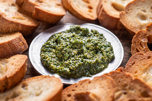 Homemade pesto sauce in a wooden bowl and ingredients for cooking on a gray background close-up. Italian food.