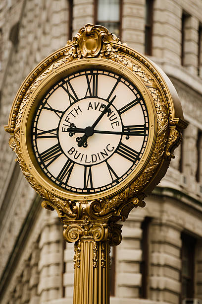 A close-up of the famous clock at 200 Fifth Avenue with the Flatiron building in the background.  The cast iron clock was built in 1909 by Hecla Iron Works and was designated as a landmark in 1981 by the New York City Landmarks Preservation Commission.