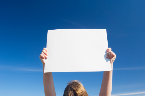 Blank white sign being held up against a clear blue sky. Space for copy.