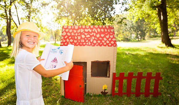 Little architect in front of playhouse Portrait of a smiling girl holding blueprint of self-made playhouse. Horizontal Shot. Please checkout our lightboxes  kids play house stock pictures, royalty-free photos & images