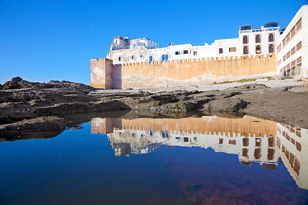 Part of the fortified wall of the old city reflected in a pool left by the receding tide. Essaouira, Morocco