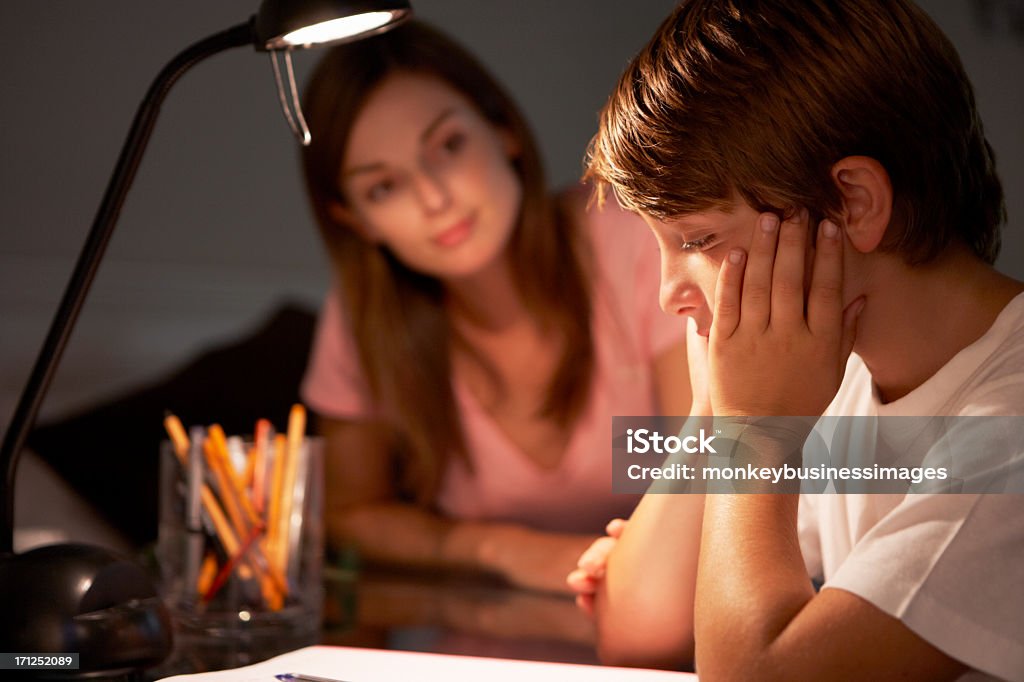 Teenage Sister Helping Stressed Younger Brother Teenage Sister Helping Stressed Younger Brother With Studies At Desk In Bedroom In Evening. Electric Lamp Stock Photo