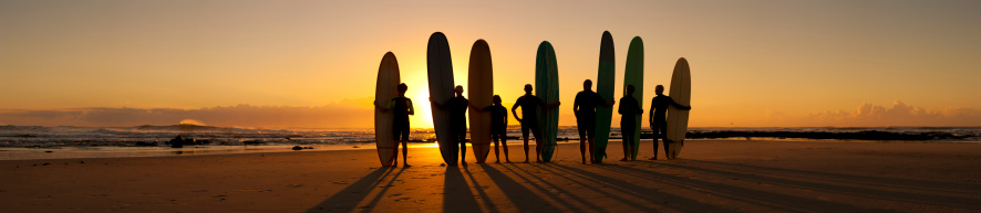 A group of longboard surfers on the beach at sunrise.