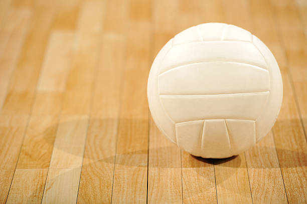 A lone white volleyball sitting on a wooden floor stock photo