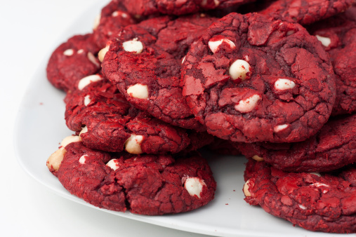Red velvet cookies with white chocolate chips on a white plate sitting on a white table.