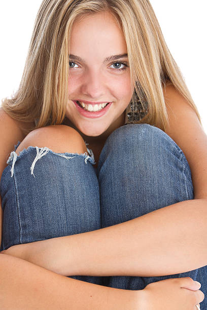 full length portrait of a blonde girl wearing casual cream shirt and blue jeans, seated pose. isolated against white background.