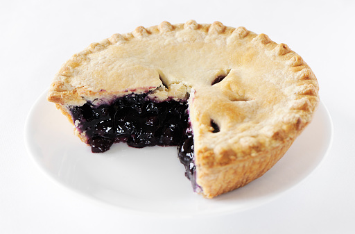 Blueberry pie with one portion missing in a white plate on  a white background.
