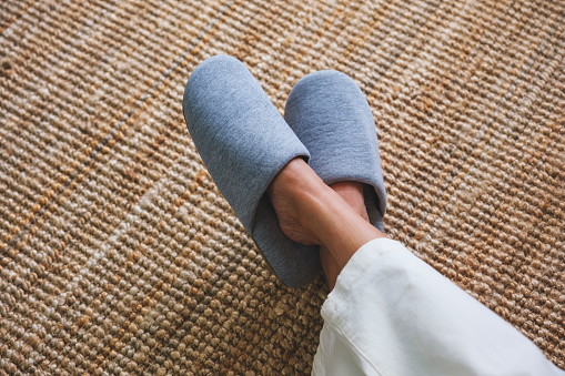 Top view image of a woman with cross legs wearing slippers at home