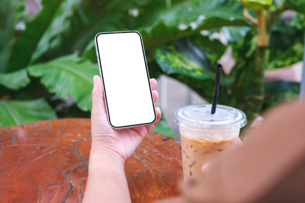 istock Mockup image of a woman holding mobile phone with blank white desktop screen while drinking coffee 1712546882