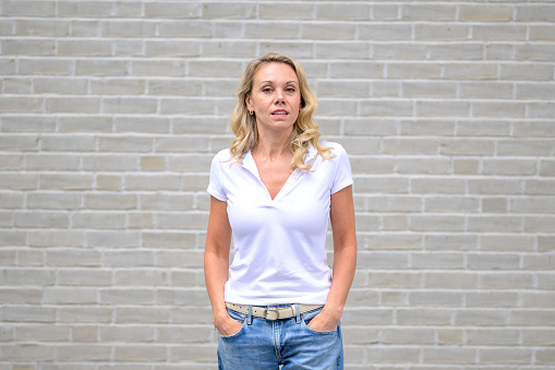 Upper body portrait of an attractive blonde woman looking at the camera with an arrogant look in front of a white brick wall